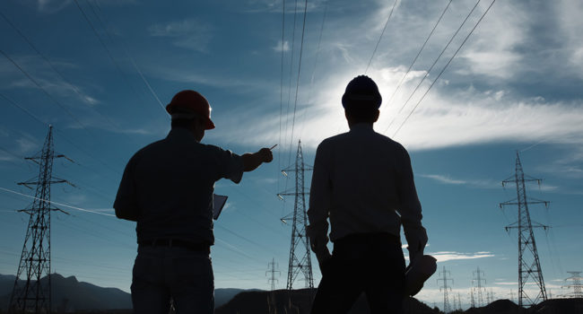 silhouette of two engineers standing at electricity station at sundown