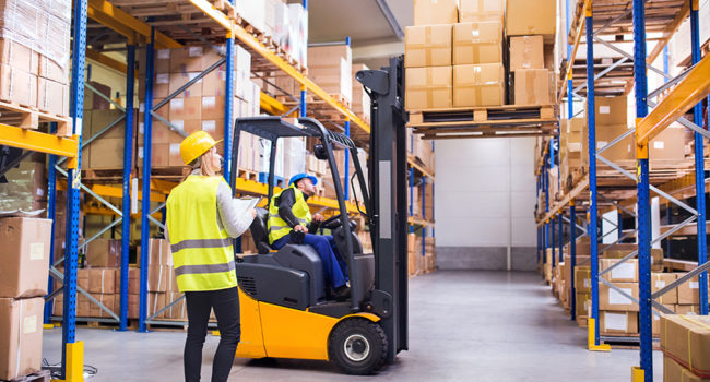 Young workers working together. Man forklift driver and a woman in a warehouse.